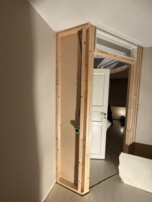 En påbörjad rivning av en vägg med synliga reglar i ett rum. En dörr står öppen mot ett annat rum, och en bit av MDF-skiva syns på golvet.