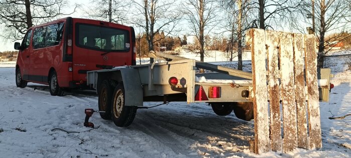 Röd skåpbil kopplad till en släpvagn på snötäckt mark, utan användning av domkraft, visar däckbyte på släpvagnen.