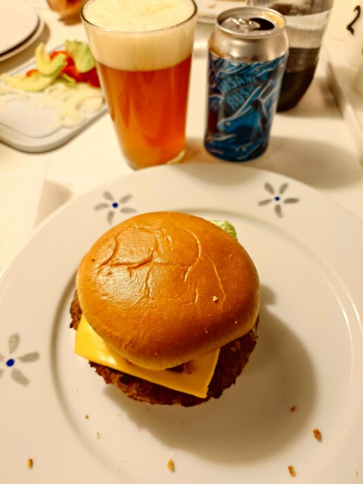 Hamburgare med ost på tallrik, med glas öl och burk i bakgrunden.