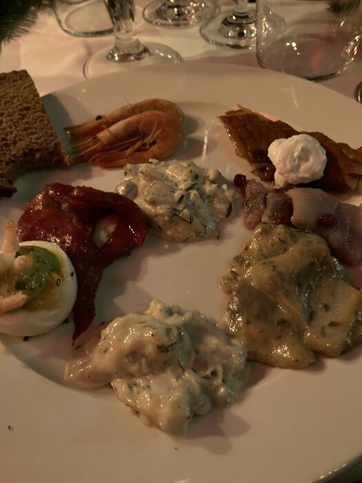 Tallrik med olika sorters sill och räkor, bröd, en skiva rökt lax samt en dessert med vispgrädde.