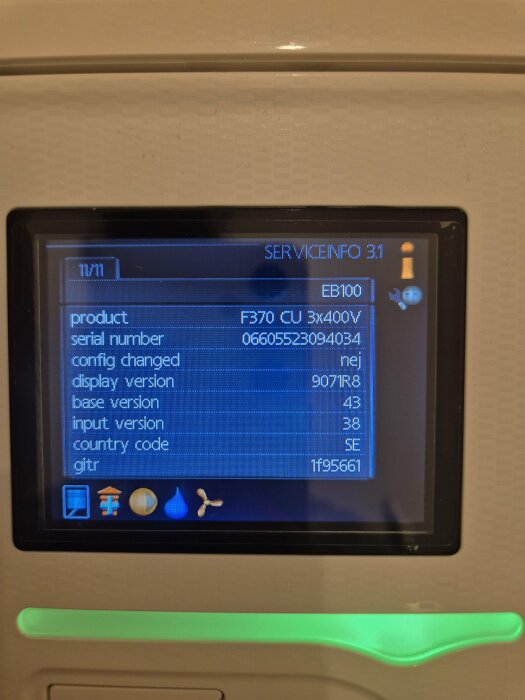 Digital kontrollpanel visar serviceinfo för värmepump, inklusive serienummer och produktkod, del av ett välisolerat husprojekt.