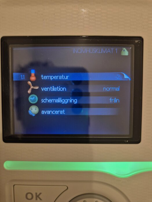 Temperaturkontroll på digital display för välisolerat hus med moderna treglasfönster, visar alternativ som temperatur, ventilation och schemaläggning.