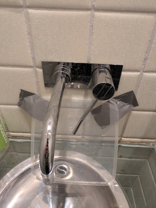 Kökskran med plastskiva fasttejpad som skvättskydd ovanför en rund diskho.