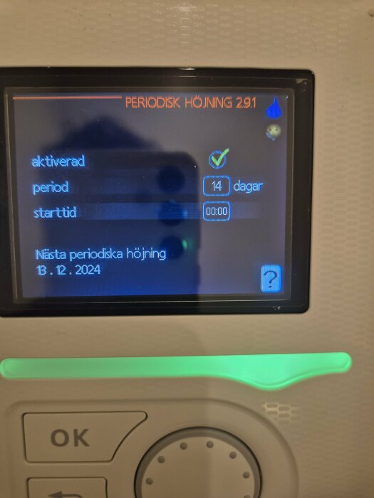 Digital termostatdisplay med inställning för periodisk höjning var 14:e dag, aktiverad. Nästa höjning 13 december 2024.