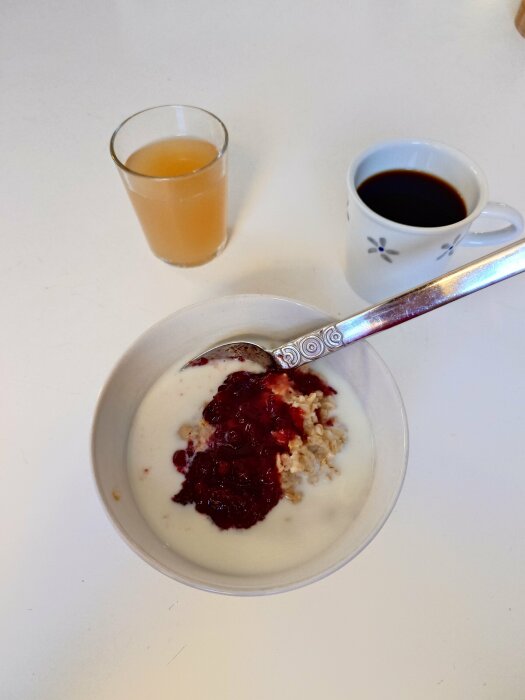 Skål med havregrynsgröt och sylt, glas med juice och kopp kaffe på ett bord.