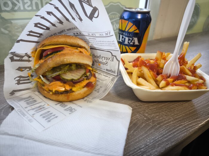 En hamburgare med ost, sallad och pickles på Elvis Burger, med en portion pommes frites med ketchup och en läskburk bredvid på bordet.