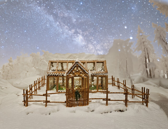 Pepparkaksväxthus med snötäckt tak och omgivning, stjärnklar himmel i bakgrunden.
