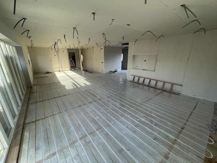 Installation av golvvärmesystem där slangen ligger i spårad plywood med aluminium för optimal värmefördelning i ett stort rum under konstruktion.