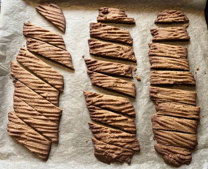 Kola- och pepparkakssnittar på bakplåtspapper, delade i diagonala bitar, med gyllenbrun färg och krispig yta.