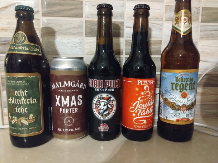 Fem flaskor julöl på en bänkskiva, inklusive olika märken såsom XMAS Porter och Bohemia Regent.