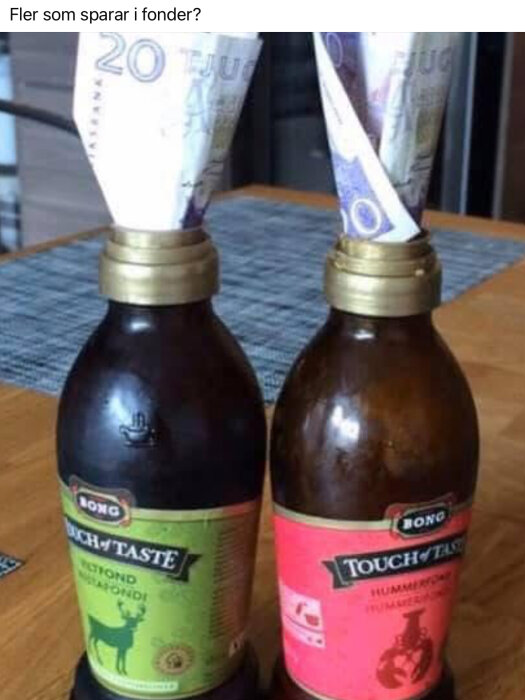 Två flaskor fond med hopvikta tjugokronorssedlar instuckna i öppningarna står på ett bord inomhus.