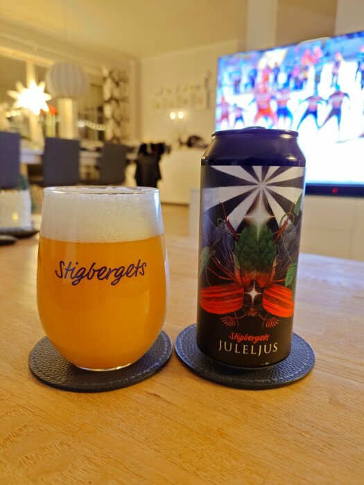 Ett glas med Stigbergets öl bredvid en burk Juleljus står på ett bord. I bakgrunden syns en TV som visar en vinterscen.