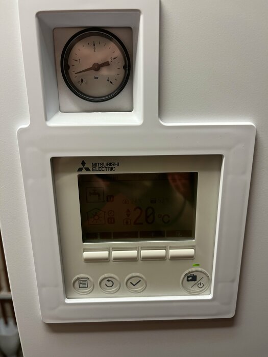 Tryckmätare och kontrollpanel på Mitsubishi Ecodan luft-vattenpump. Display visar temperatur och olika knappar finns under.