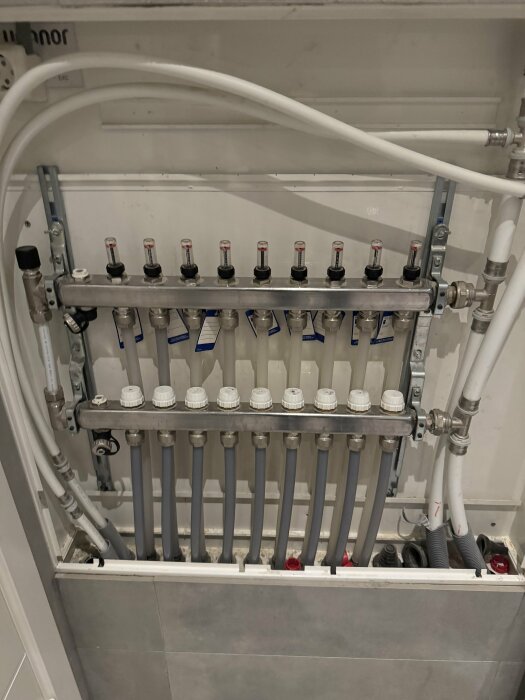 Rörsystem för golvvärmeinstallation med flera anslutningar och ventiler i ett skåp.