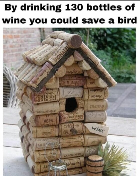 Fågelholk byggd av vinkorkar med text: "By drinking 130 bottles of wine you could save a bird". Holken står på ett bord med växt intill.