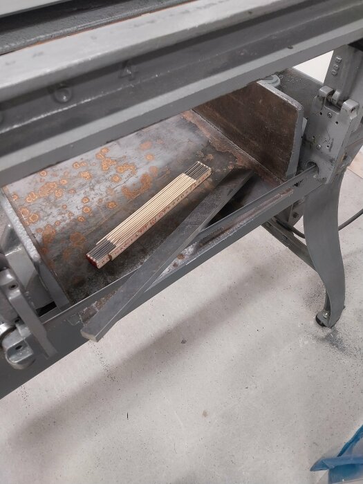 Rostig metallarbetsbänk med ett hopfällt tomstockmått placerat ovanpå.