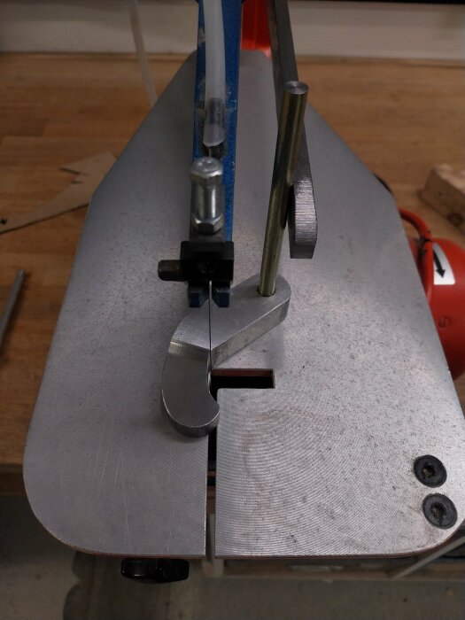 En hemmabyggd press för figursågning på arbetsbänk, med en metallarm monterad bredvid ett sågbord för bättre stabilitet.