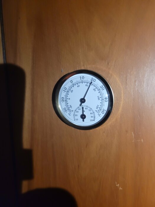 Kombinerad temperatur- och fuktighetsmätare monterad på en träpanel.