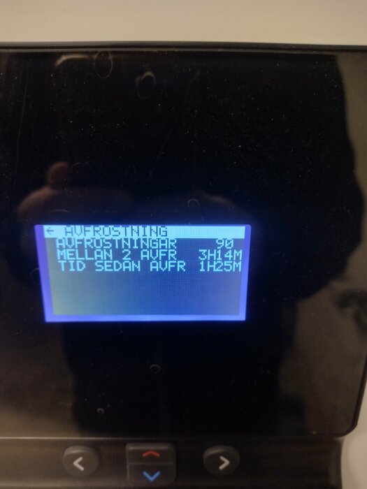 Display på värmepump som visar avfrostningsdata med text: "AVFROSTNING", antal avfrostningar, tid mellan avfrostningar och tid sedan senaste avfrostning.