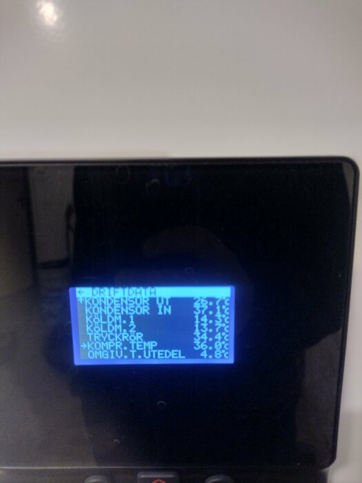 Närbild på skärm med driftdata från en värmepumps utedel som visar olika temperaturvärden, exempelvis kondensor och omg.t.utdel.