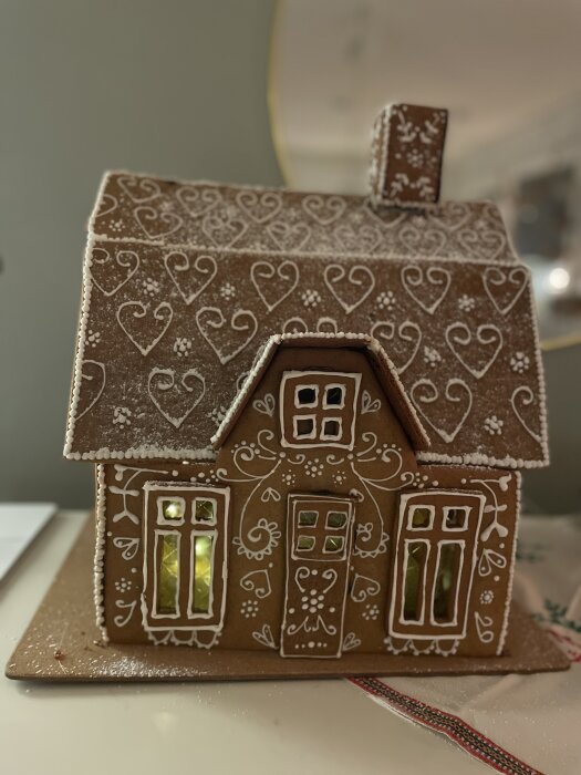 Pepparkakshus dekorerat med kristyr och hjärtmönster, med belysning inuti.