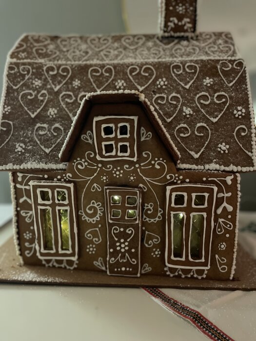 Pepparkakshus dekorerat med vita kristyrhjärtan och mönster, föreställande ett hus med fönster och en dörr, bakat av dottern Ebba.