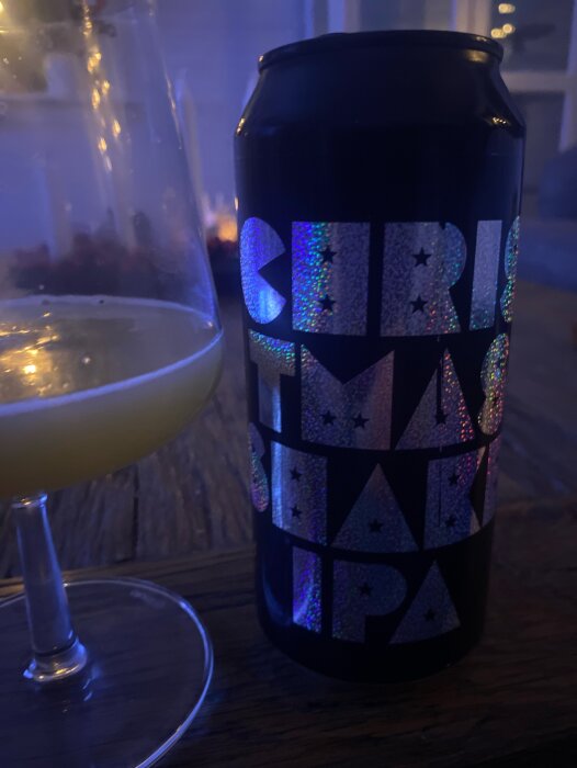 Svart burk med texten "Christmas shake IPA" bredvid ett glas med ljus öl på ett bord.