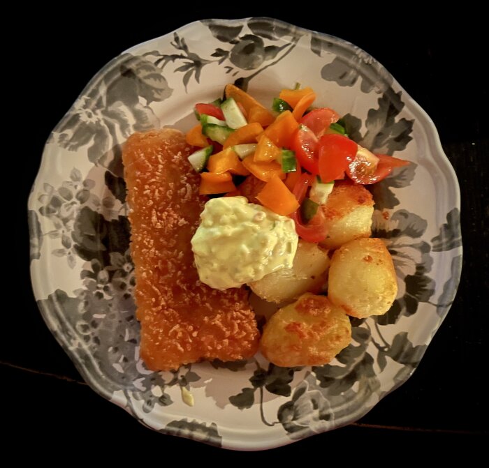 Panerad torsk med remouladsås, ugnstekt potatis och sallad på en blommig tallrik.