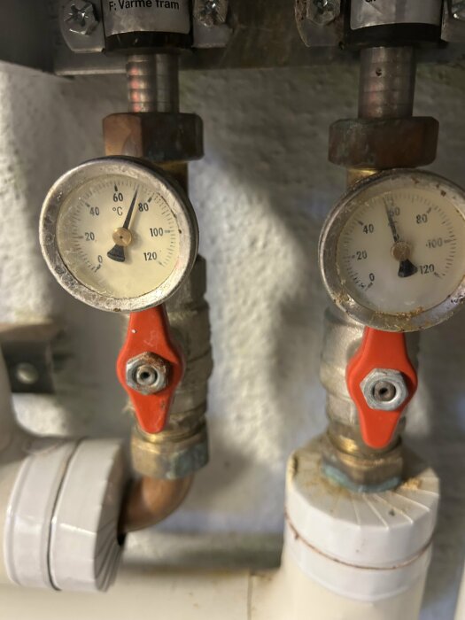Två tryckmätare i ett värmesystem som visar lågt tryck, med röda ventiler under varje mätare.