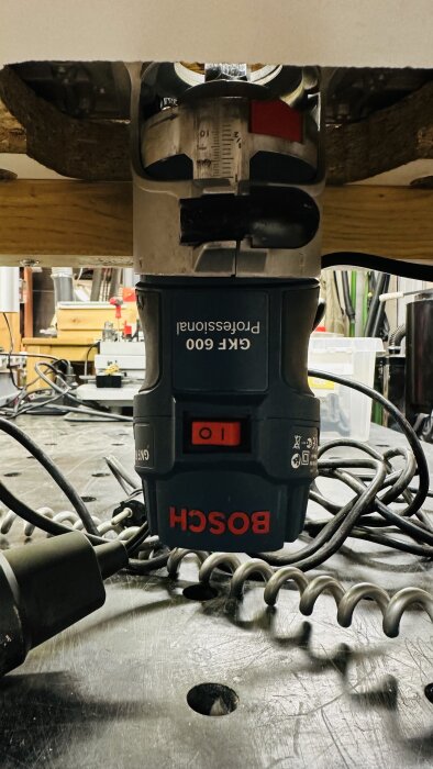 Bosch GKF 600 fräs monterad i ett robust fräsbord av massiv ek och spånskiva, med verktyg och kablar i bakgrunden.