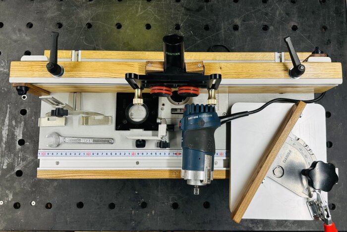 Verktygsinstallation med Festool-dammsugare, Bosch router och skiftnyckel på arbetsbänk med måttband.