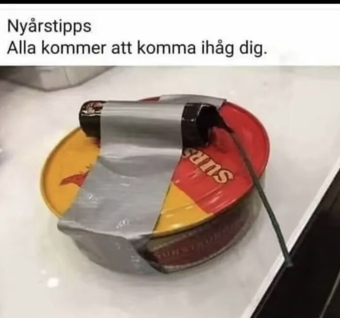 En burk surströmming med en fäst fyrverkeripjäs med silvertejp.