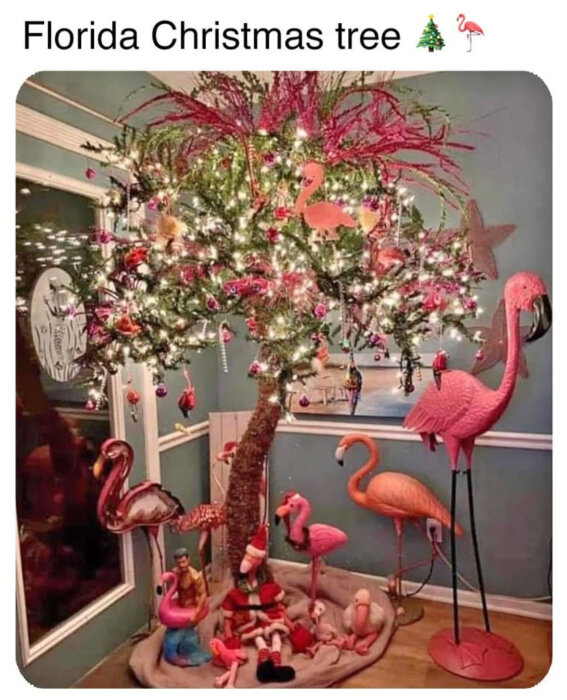 En julgran dekorerad med rosa flamingos och julbelysning i ett rum med gröna väggar och flamingofigurer omkring.