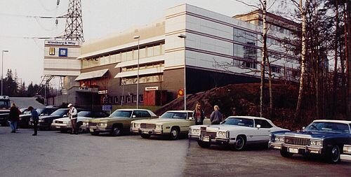 Byggnad med Klintberg & Way-logga, flera klassiska amerikanska bilar parkerade framför, människor interagerar.