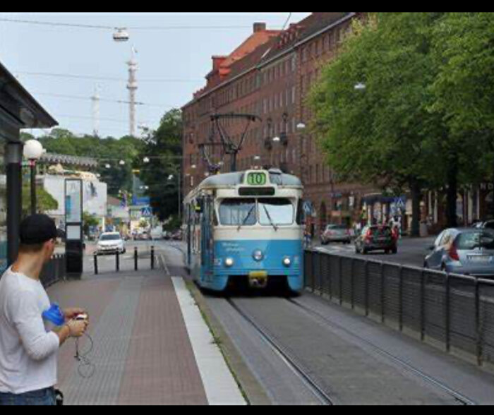 Blå spårvagn nummer 10 på en gata, en person står vid hållplatsen i stadsmiljö.