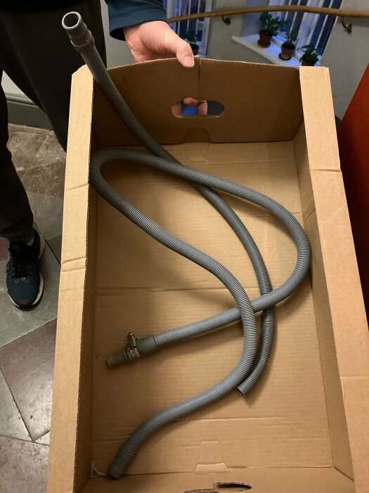 Gammal grå slang i en kartong, hålls av en person, visas för att demonstrera dess styvhet jämfört med en nyare slang.