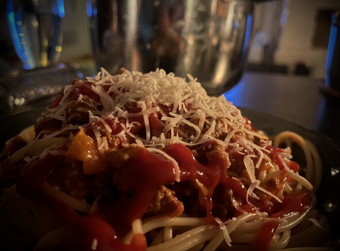 Tallerken med spaghetti toppad med köttfärssås och riven parmesanost, fotograferad i närbild.