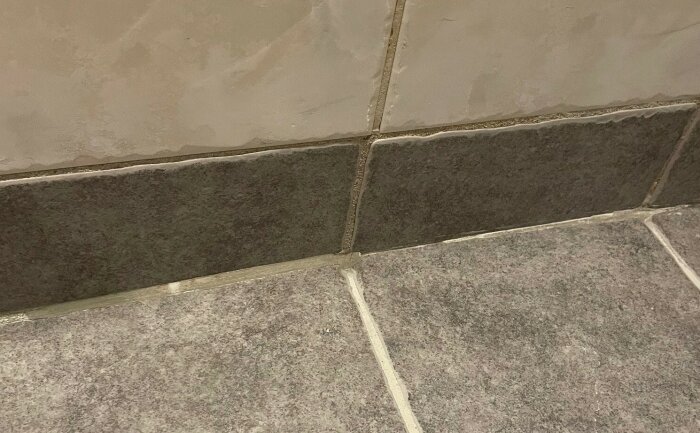 Närbild av kakelplattor i hörnet där golv och vägg möts, visar fogarna tydligt för diskussion om applicering av silikon.