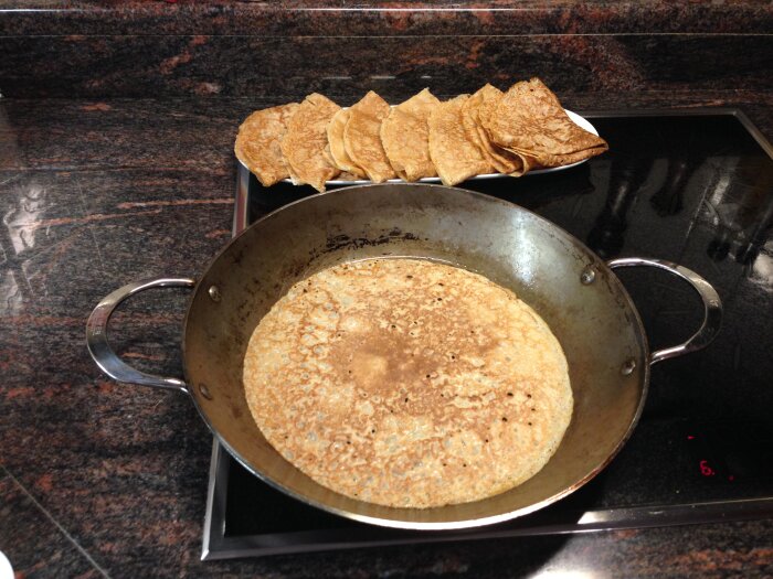 Stekpanna med pannkaka på glaskeramikhäll, fler pannkakor bredvid.