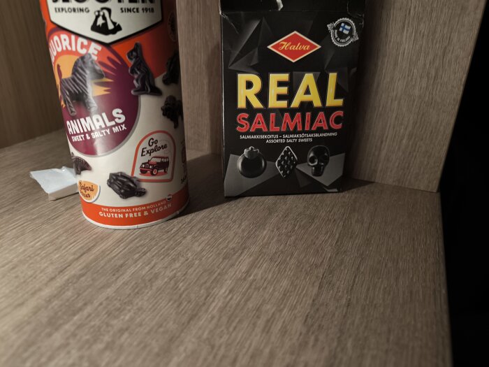 Två förpackningar lakrits: en med texten "Liquorice Animals" och en med "Real Salmiac", stående på ett träbord.