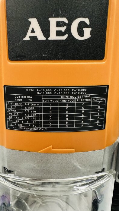 AEG OF 2050 E överhandsfräs med varvtals- och materialinställningstabell på en orange bakgrund.