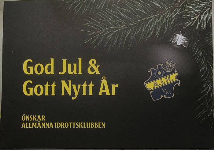 Julkort med texten "God Jul & Gott Nytt År" och Allmänna Idrottsklubbens logotyp, med en grankvist och julkula i bakgrunden.