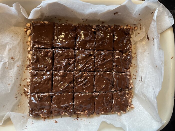 Hemgjord chokladtäckta dessertbitar, liknande rocky road, skurna i lika stora fyrkanter i en pappersklädd form.