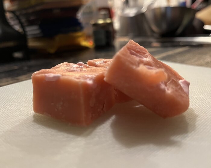 Tärningar av skumtomtefudge ligger på en vit skärbräda, del av ett julgodisprojekt i ett kök.