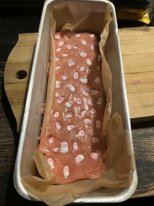 Rosa skumtomtefudge med vita och rosa godisbitar i rektangulär form, stående i en brödform med bakplåtspapper.