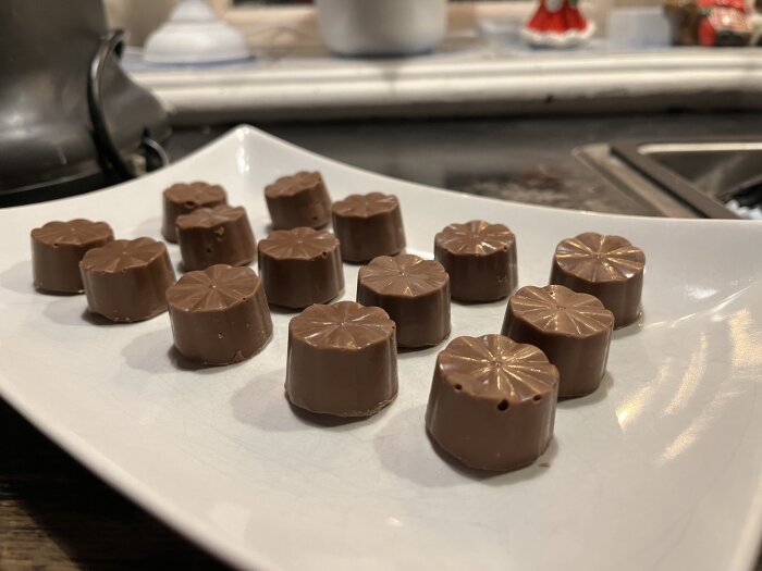 Praliner med chokladöverdrag ligger på en vit tallrik i ett kök med bänkskiva i bakgrunden.