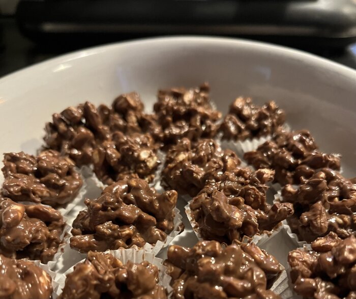 Chokladtäckta puffgodisklumpar på vit tallrik, en del av en julgodistillverkning med krokant och dajmchoklad.