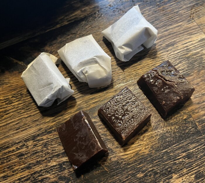 Hemgjord chokladkola och kolabitar inslagna i papper på ett träbord.