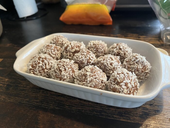 Hemgjorda kokosbollar i en vit ugnsform på ett mörkt träbord.