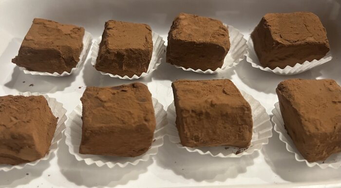 Chokladpraliner med pudrad yta i vita pappersformar på ett fat.
